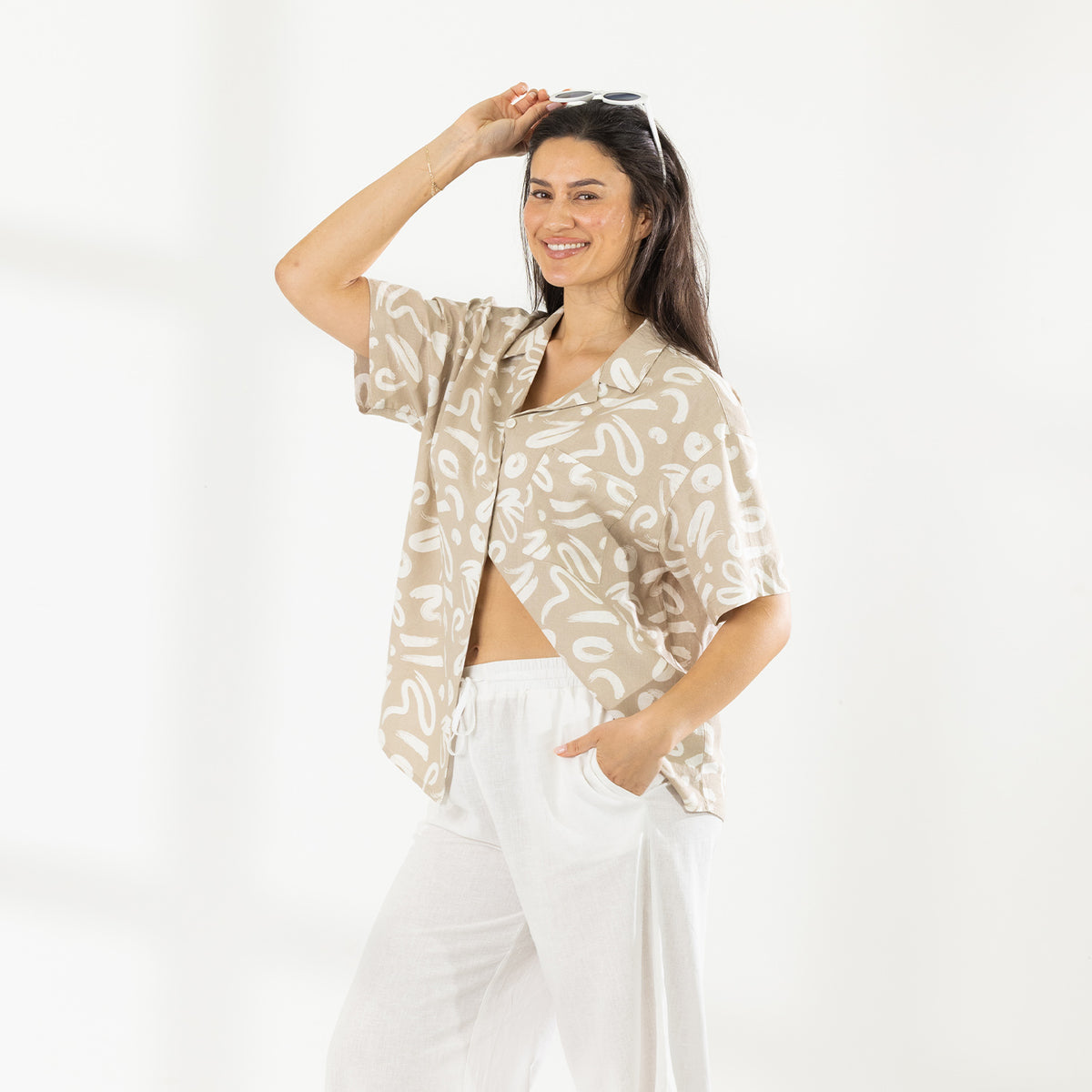 Model wearing the Cove Breeze Shirt in Natural with white pants and sunglasses resting on her head.