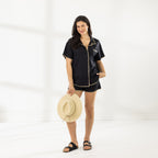 Full-length view of model wearing the Cove Breeze Stitch Shirt in Black with matching shorts and holding a straw hat.