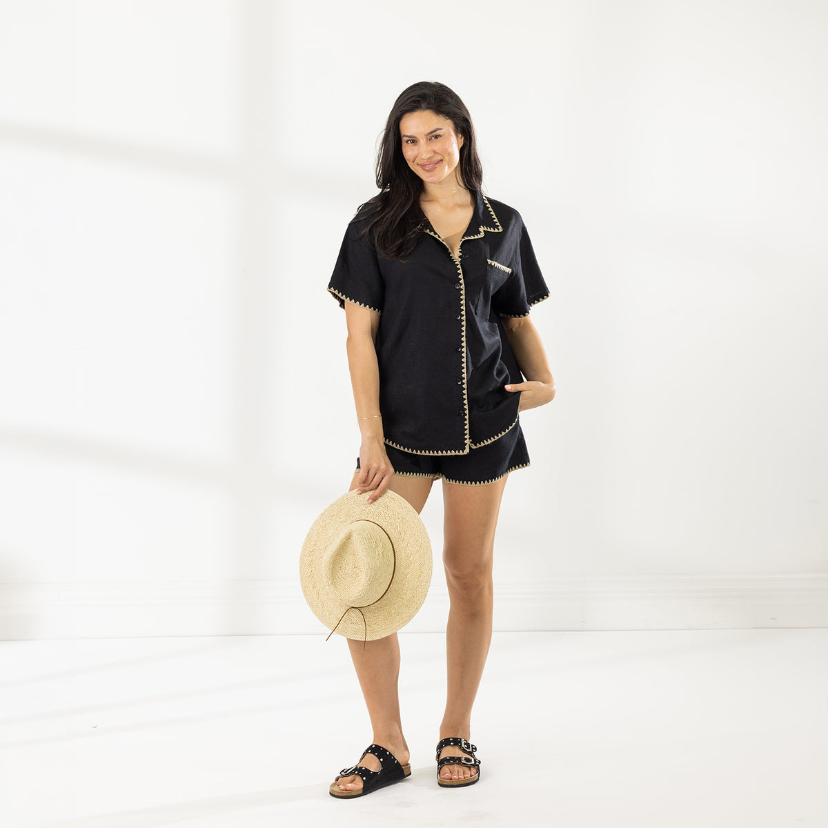 Full-length view of model wearing the Cove Breeze Stitch Shirt in Black with matching shorts and holding a straw hat.