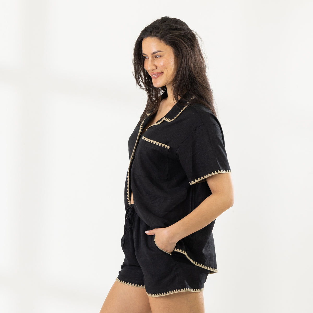 Side view of the model wearing the Cove Breeze Stitch Shorts in Black with the matching shirt, showing the relaxed fit and contrast beige stitching.