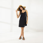 Full-length view of model wearing the Cove Stitch Slip Dress in Black with a wide-brim straw hat and sandals.