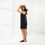 Side view of model wearing the Cove Stitch Slip Dress in Black with a wide-brim straw hat.