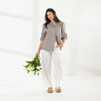 Full-length view of the model wearing the Cove Breeze Collarless Shirt in Chocolate Check with ivory pants, holding a bouquet of white flowers.