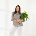 Model wearing the Cove Breeze Collarless Shirt in Chocolate Check with ivory pants, holding a bouquet of white flowers.