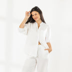 Model wearing the Cove Breeze Collarless Shirt in Ivory with coordinating ivory pants, posing with one hand in her pocket.