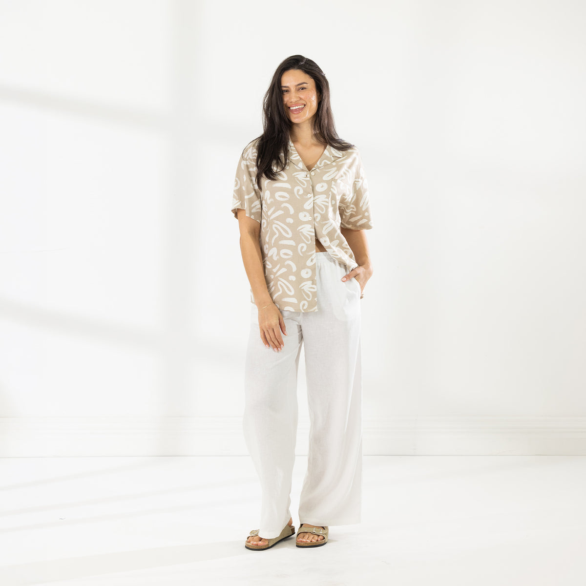 Full-length view of the Cove Breeze Wide Leg Pants in Ivory, styled with a printed short-sleeve shirt and sandals.