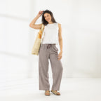 Full-length view of the Cove Wide Leg Pants in Chocolate styled with an ivory sleeveless top and woven tote bag.