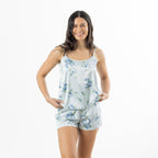 Front view of a woman modelling the pale blue satin floral cami pyjama set, holding the hem of the camisole to show the relaxed fit.