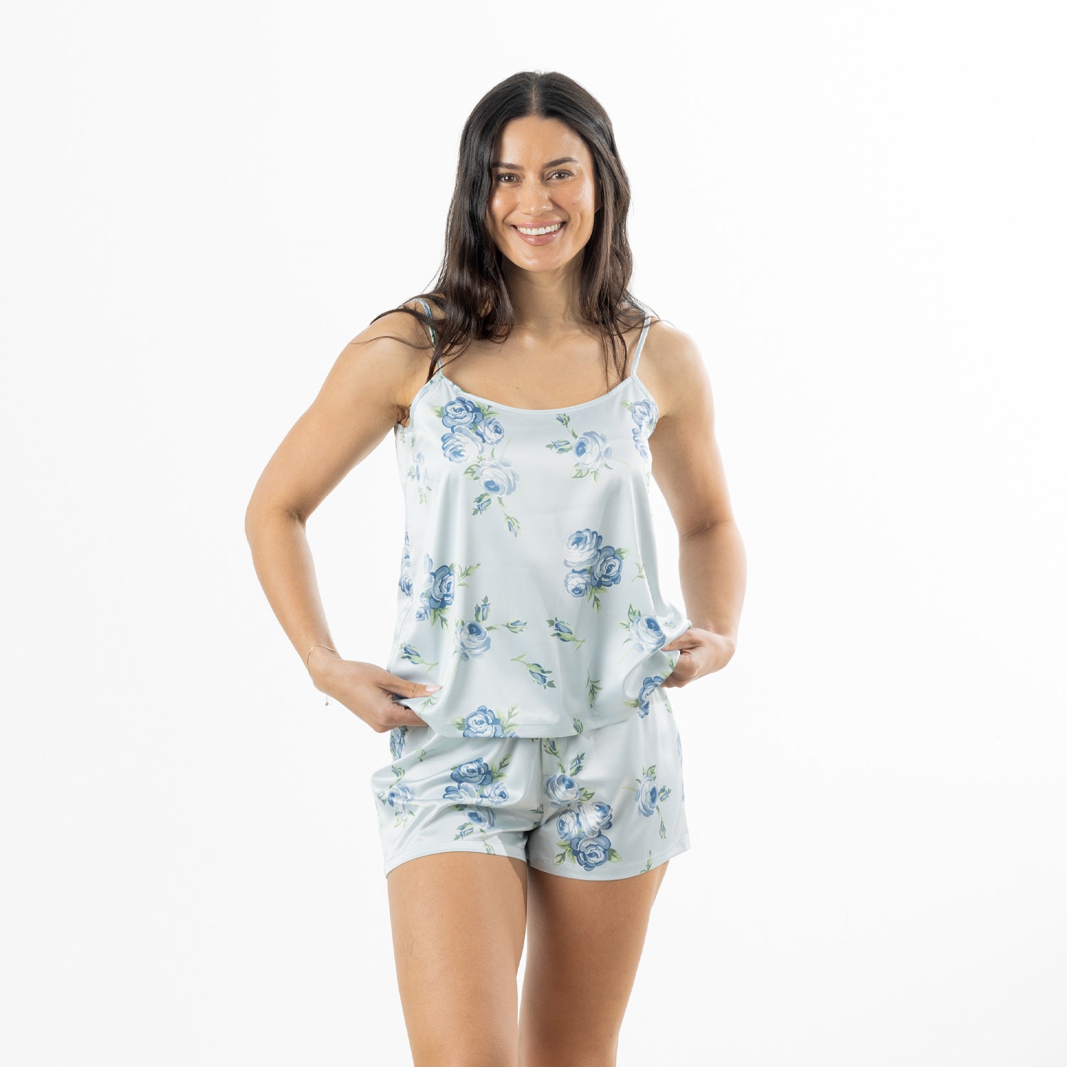 Front view of a woman modelling the pale blue satin floral cami pyjama set, holding the hem of the camisole to show the relaxed fit.