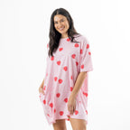 Woman modelling a soft pink oversized sleep tee with an all-over red heart-shaped lollipop print and short sleeves against a white background.