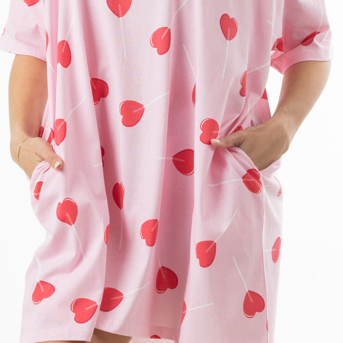 Close-up of the soft pink oversized sleep tee showing the red heart-shaped lollipop print and roomy side pockets.