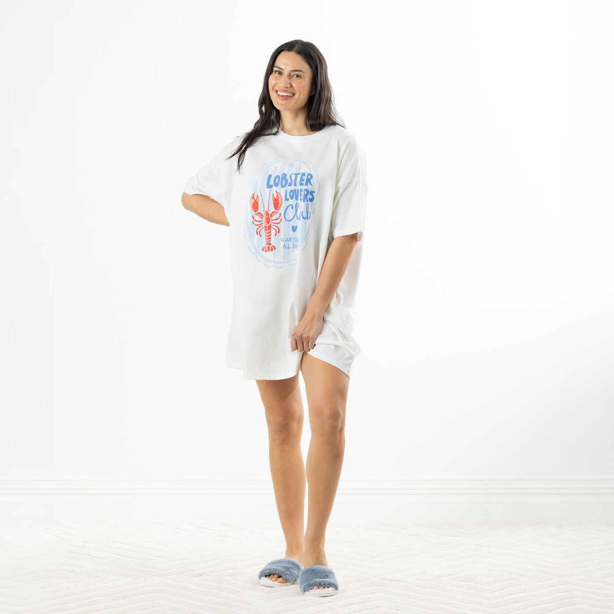 Full-length view of the white Lobster Lovers Club oversized sleep tee styled with fluffy blue slippers against a white studio background.