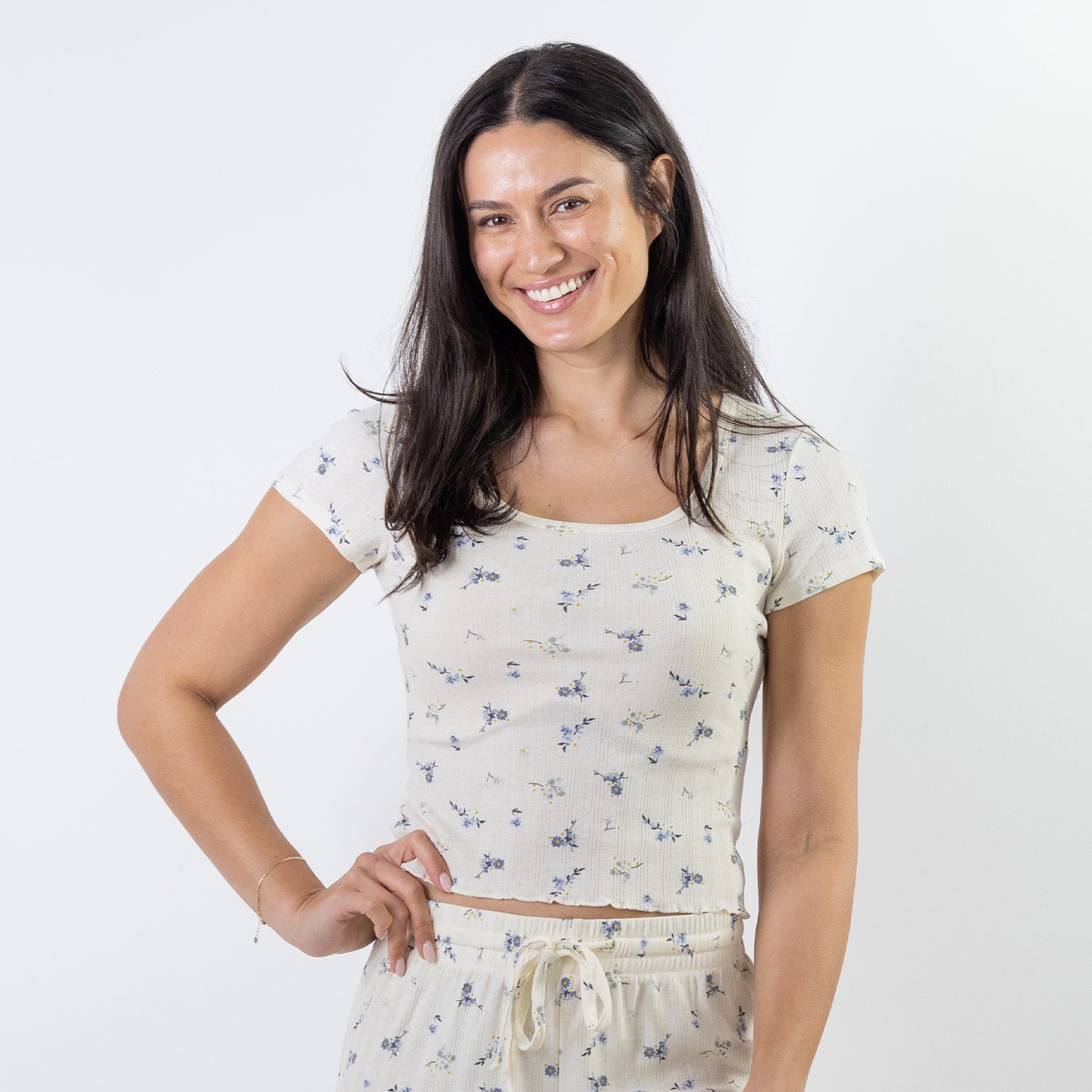 A woman modeling a matching short-sleeve pj top and drawstring shorts set in a light cream color with a small blue floral print, against a plain white studio background.