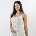 A woman with long dark hair wearing a cream-colored spaghetti-strap pj cami with a small blue and yellow floral print, photographed against a solid white studio background.