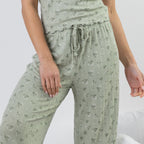 A close-up of a person wearing light sage green drawstring lounge pants with a small all-over floral print, paired with a matching top.