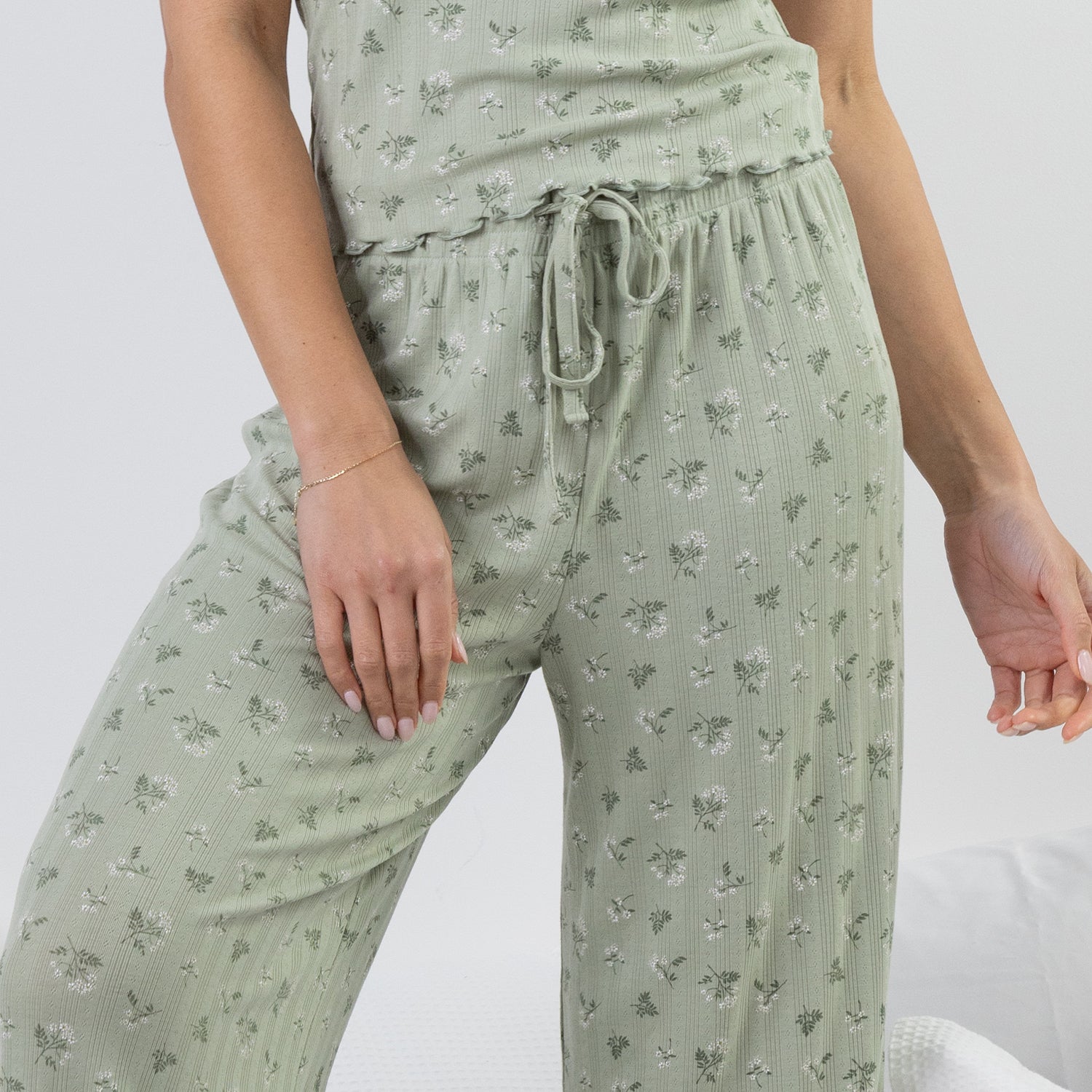 A close-up of a person wearing light sage green drawstring lounge pants with a small all-over floral print, paired with a matching top.