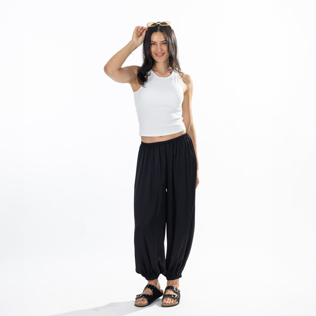 Full-length view of a model wearing black Simple & Sunday Lounge Satin Pants styled with a white sleeveless top and black sandals.
