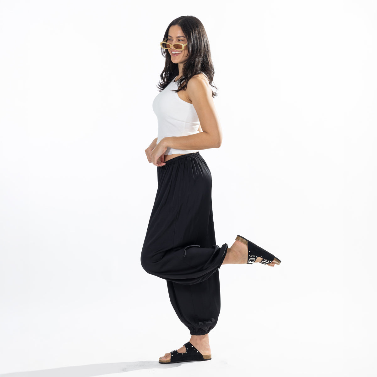 Side view of a model wearing black Simple & Sunday Lounge Satin Pants with a loose fit and gathered ankle cuffs.