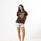 Model wearing the chocolate brown bb&b Sleep Heart Toast Print Sleep Tee with light blue striped pyjama shorts against a white background.
