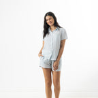 Model wearing the bb&b Sleep Sea Shells Short Sleeve PJ Set in Denim, featuring a short-sleeve button-up shirt and matching shorts with a white coastal print.