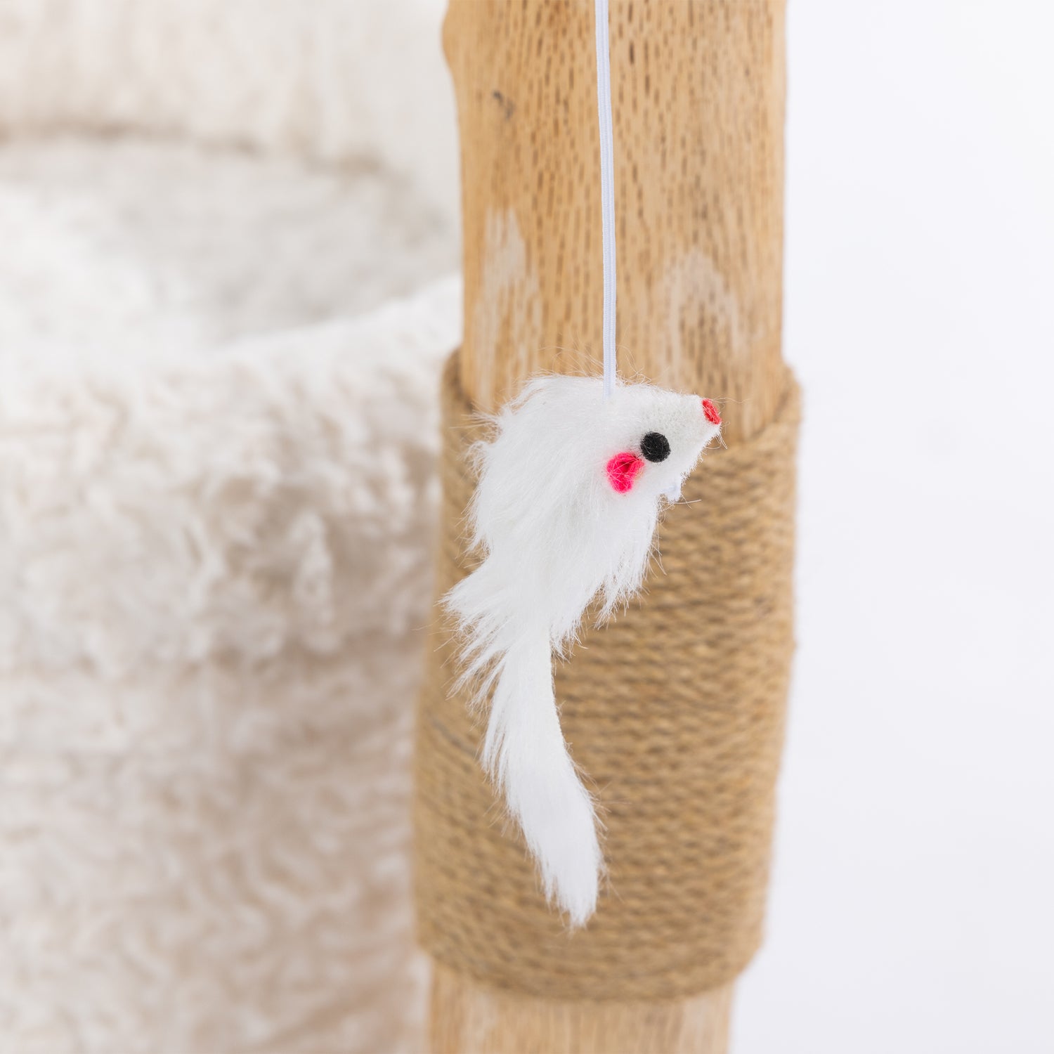 Close-up of the white plush mouse toy with pink ears hanging from the elevated perch of the cream cat scratcher.