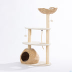 Angled front view of the natural woven cat tower featuring the plush top basket, woven hideaway, sisal scratching posts, climbing rope, and hanging pom-pom toys displayed on a white background.