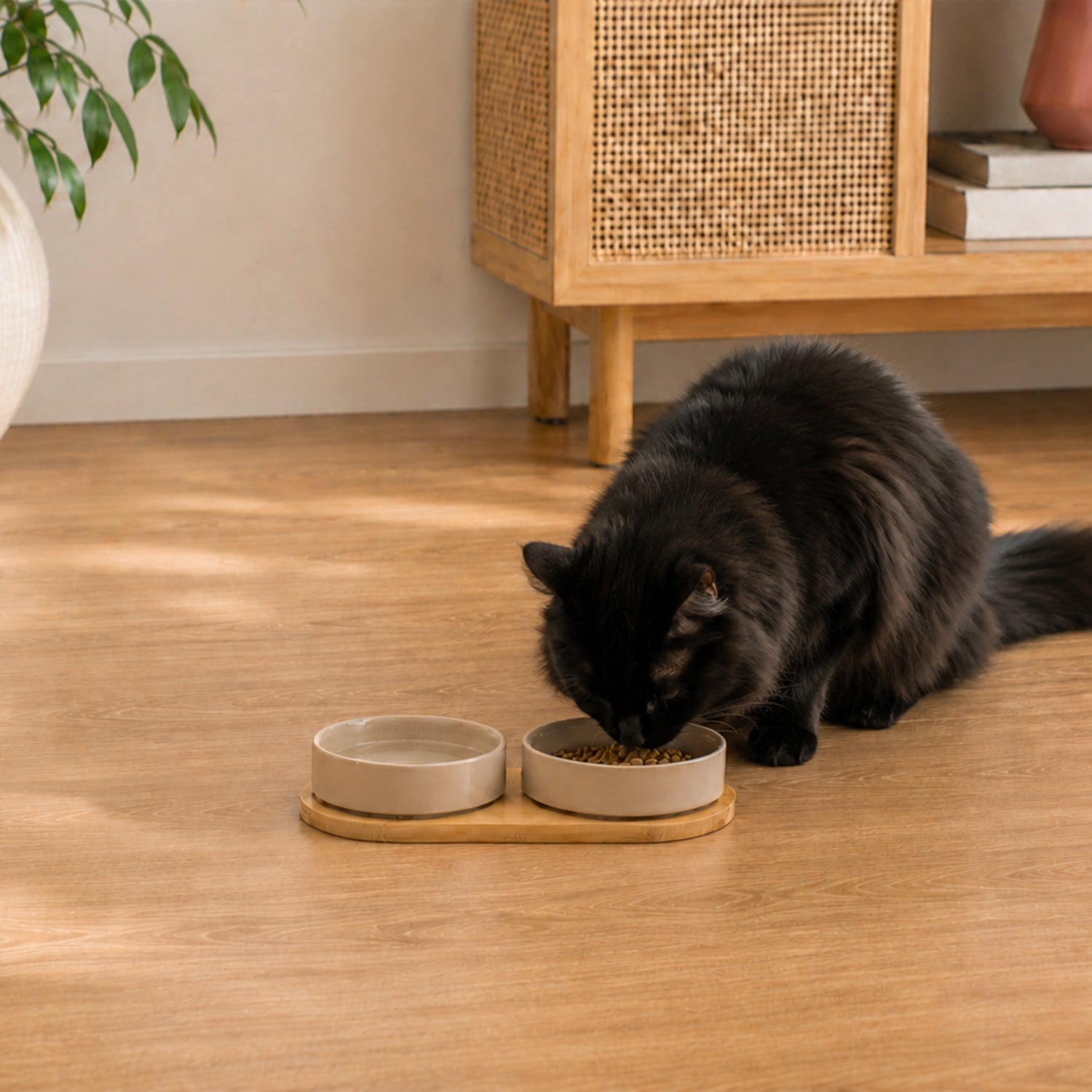 Fluffy black cat eating from a mushroom-coloured ceramic pet bowl set on a bamboo holder in a warm home interior.