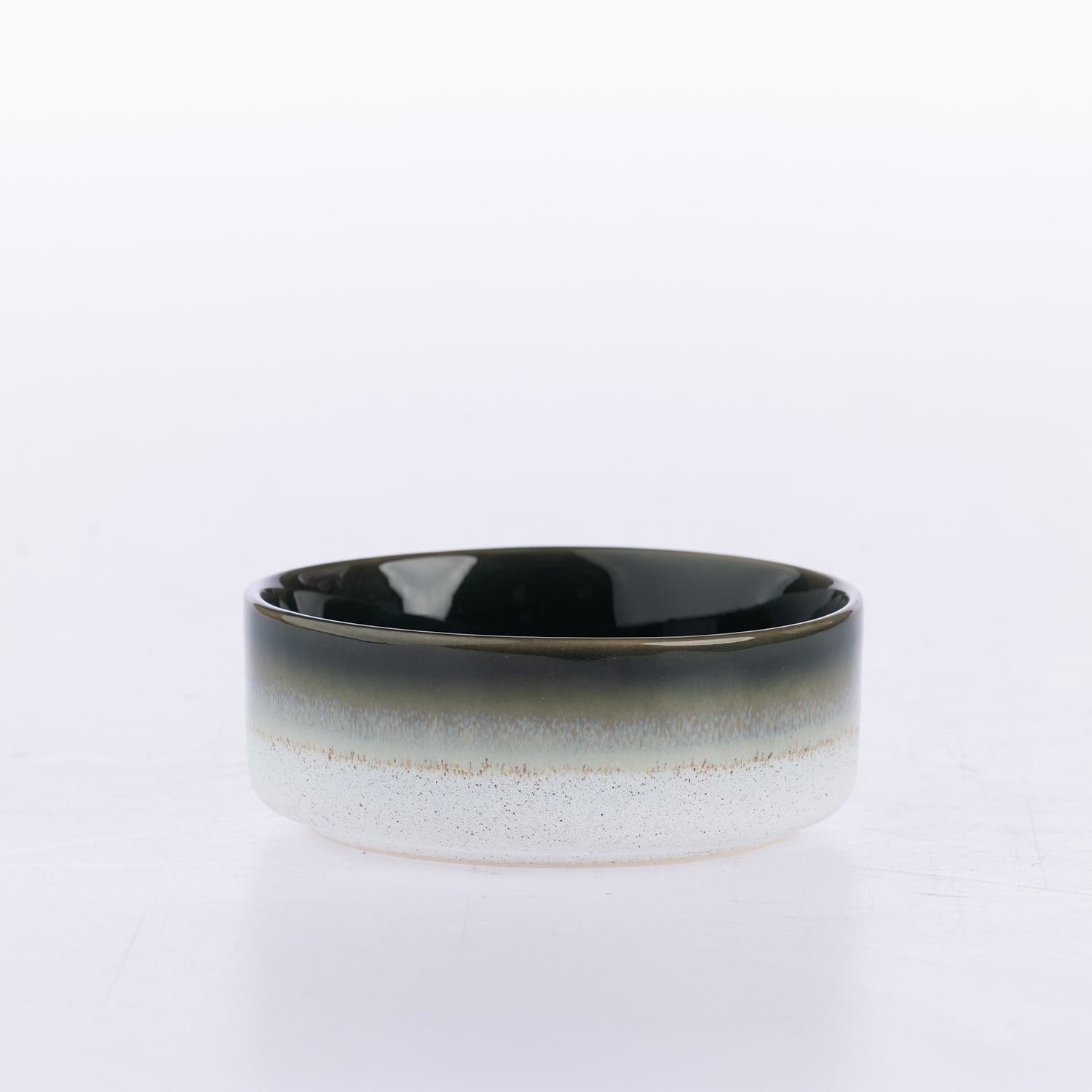A wide ceramic bowl with a glossy black interior and a speckled white exterior featuring a subtle gold band around the middle, set against a plain white background.