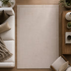 Gracious Living Sabrina Ivory Area Rug with a soft plain design and subtle border detail, styled in a contemporary living room with warm timber flooring, a cream sofa and wooden furniture.