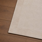 Close-up of the Gracious Living Sabrina Ivory Area Rug showing the soft textured pile, stitched border detail and rounded corner on warm timber flooring.