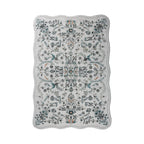A rectangular area rug with scalloped edges, featuring an intricate floral and botanical damask pattern in muted blue, gray, black, and subtle orange accents on a light gray background.
