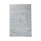 A rectangular area rug with a traditional floral pattern in shades of blue, gray, and beige on a light off-white background, shown flat against a white studio backdrop.