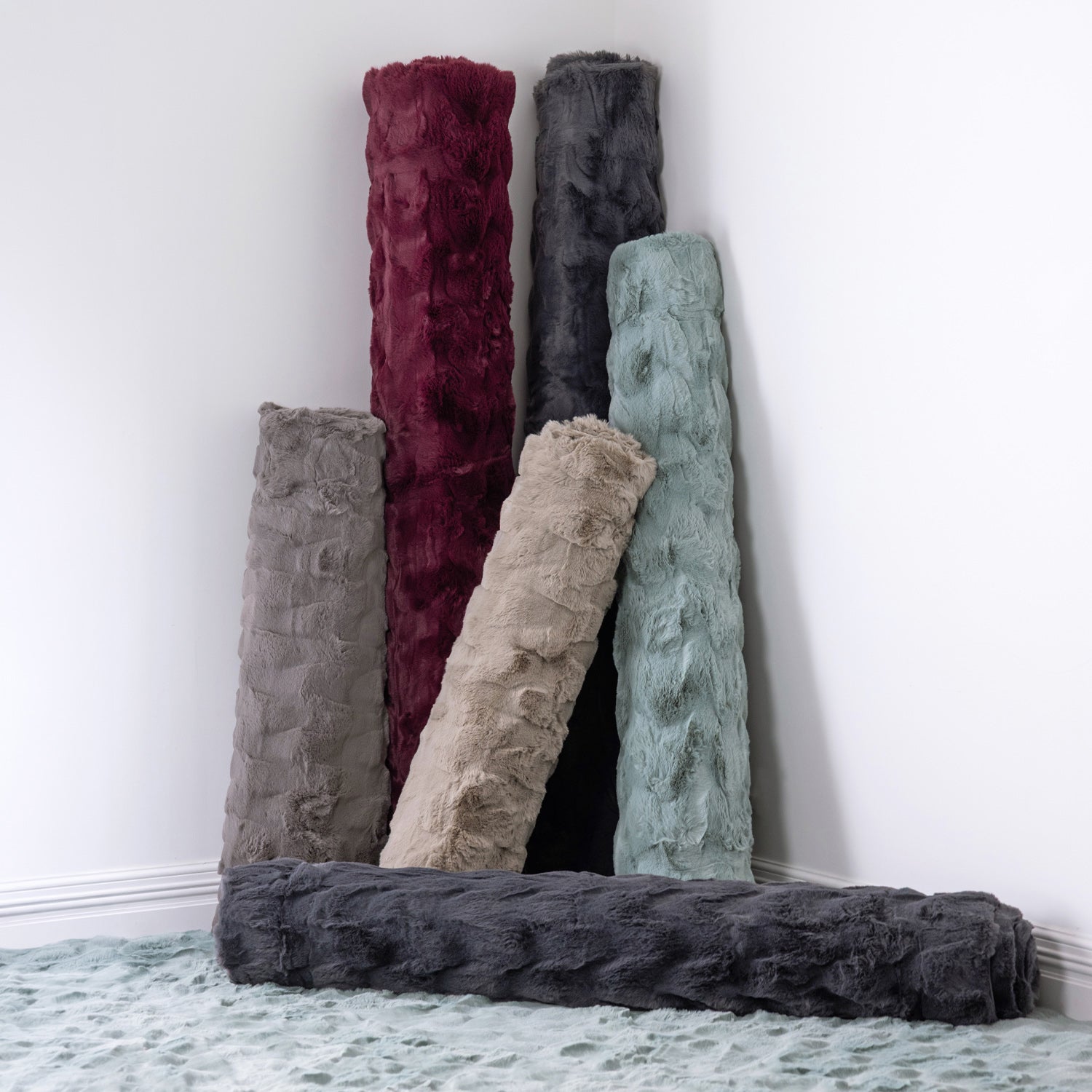 Rolled faux fur rugs in Berry, Charcoal, Sage, Taupe and Silver displayed together to showcase the available colour range.