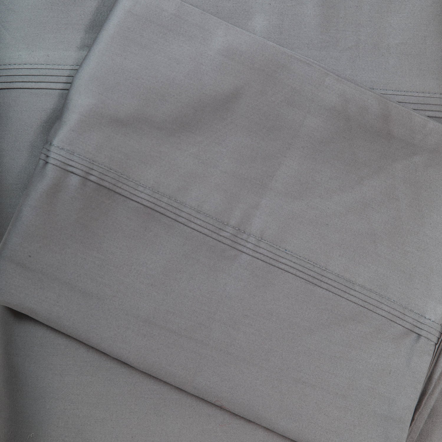 A close-up of crisp grey sateen bed sheets showcases its smooth, lustrous finish and refined stitched cuff detailing for a timeless, luxurious look.