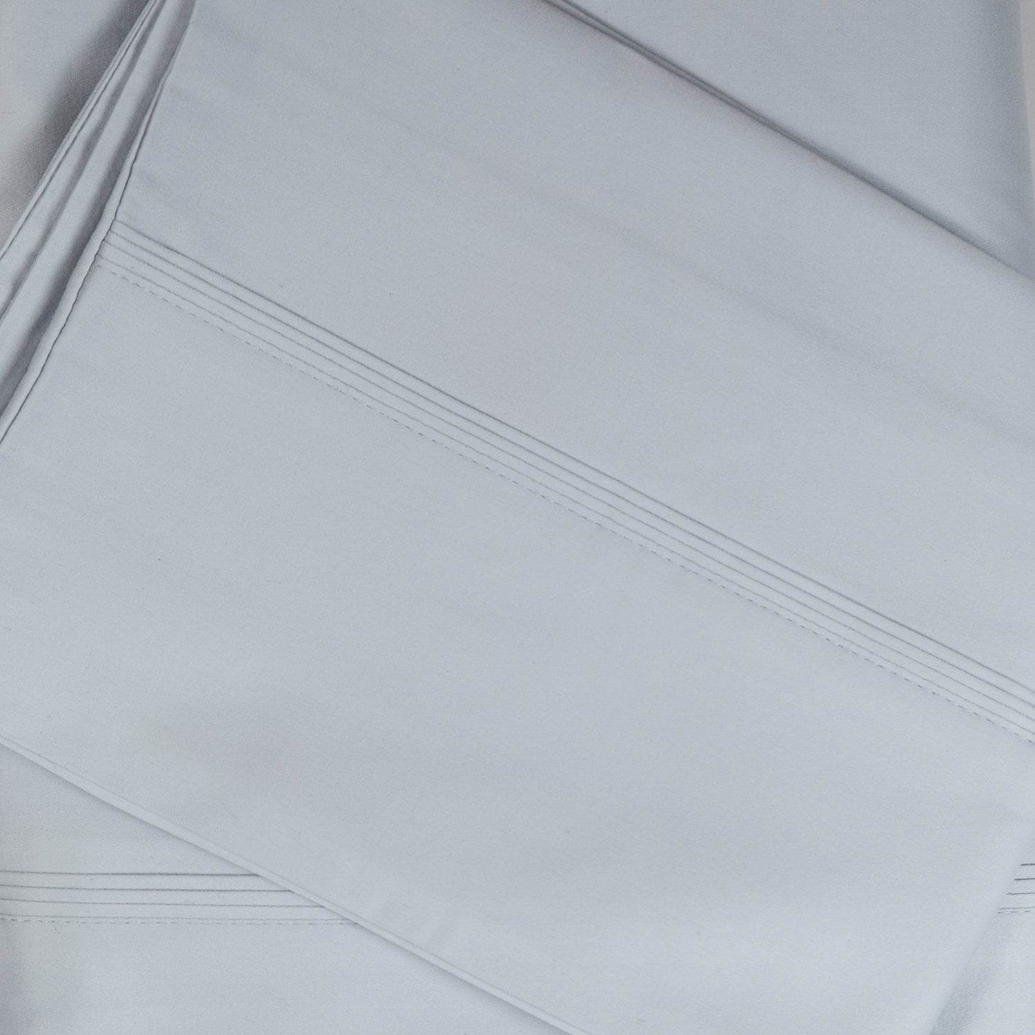 A close-up of crisp ice blue sateen bed sheets showcases its smooth, lustrous finish and refined stitched cuff detailing for a timeless, luxurious look.