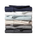 A neatly stacked collection of silky sheet sets in assorted neutral and contemporary colours showcases their smooth finish and elegant stitched cuff detailing.