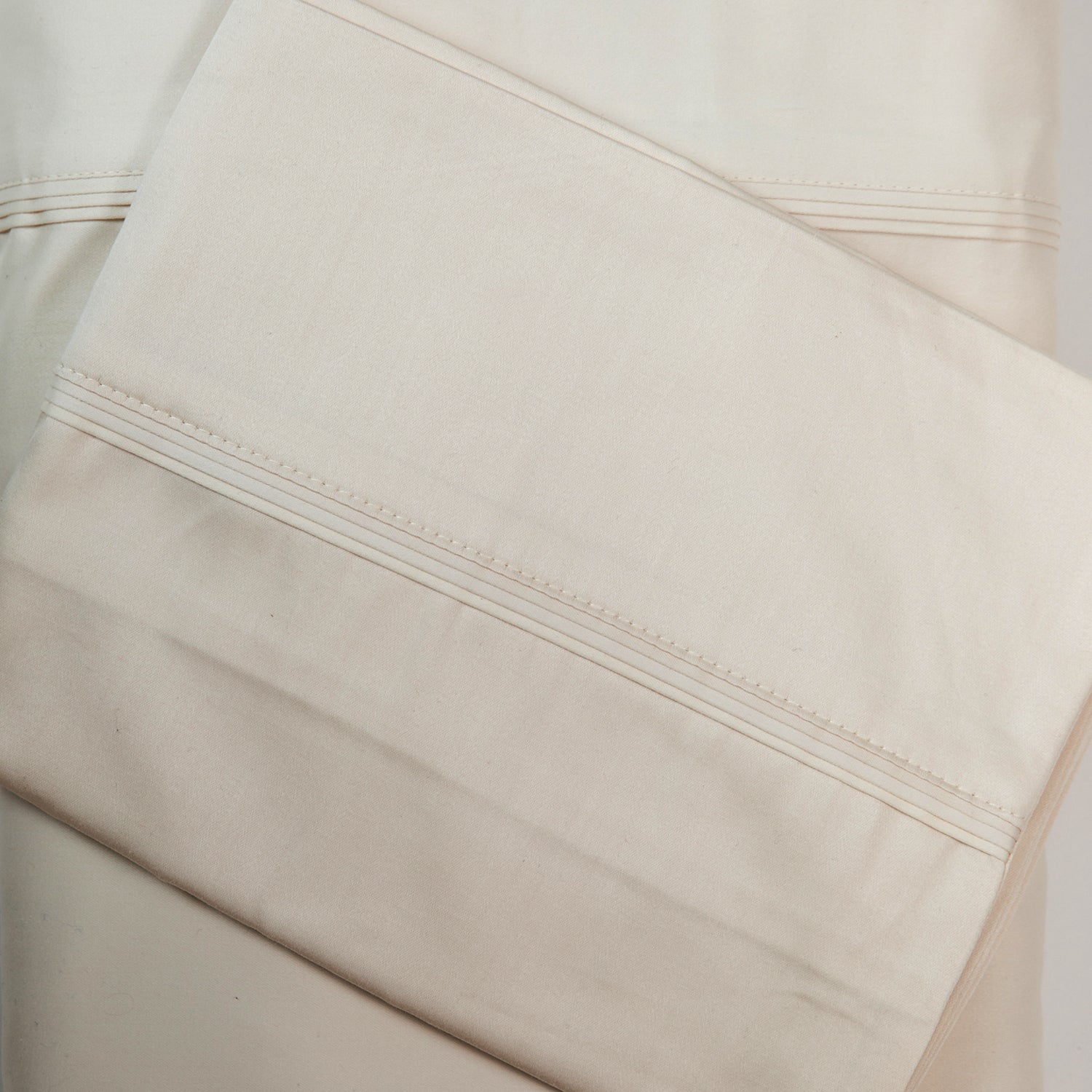 A close-up of ivory sateen bed sheets showcases its smooth, lustrous finish and refined stitched cuff detailing for a timeless, luxurious look.