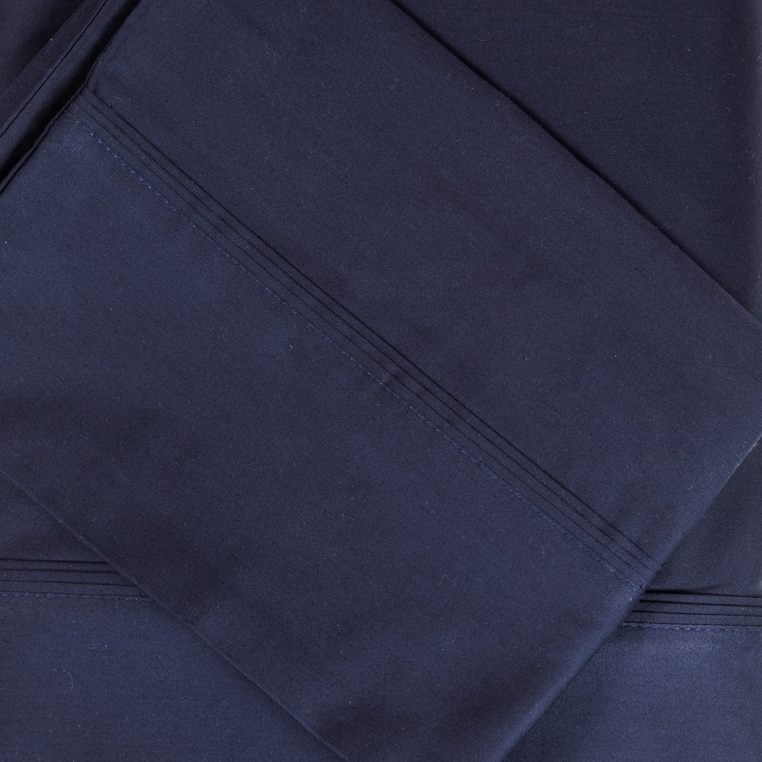 A close-up of navy sateen bed sheets showcases its smooth, lustrous finish and refined stitched cuff detailing for a timeless, luxurious look.