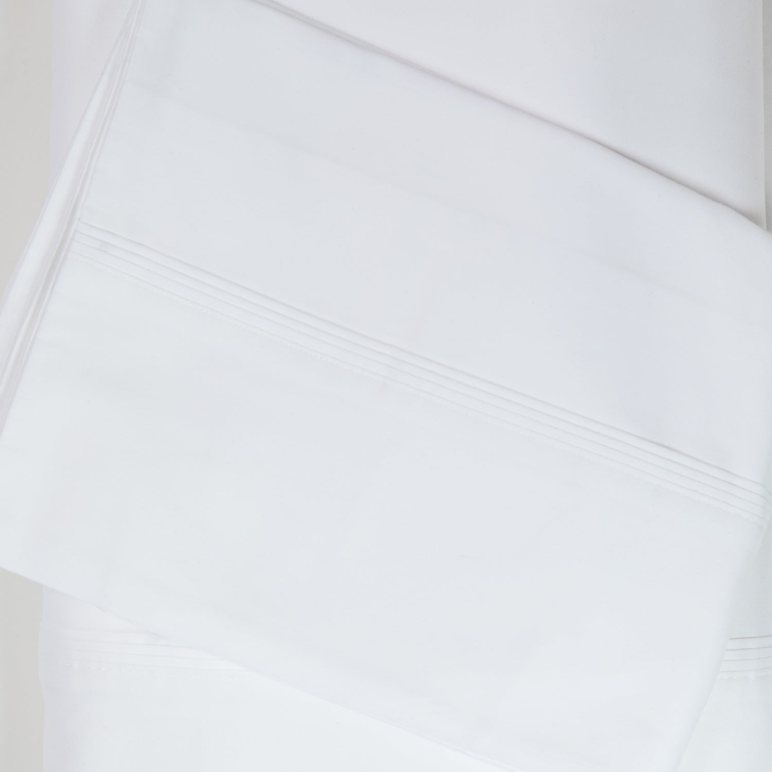 A close-up of crisp white sateen bed sheets showcases its smooth, lustrous finish and refined stitched cuff detailing for a timeless, luxurious look.