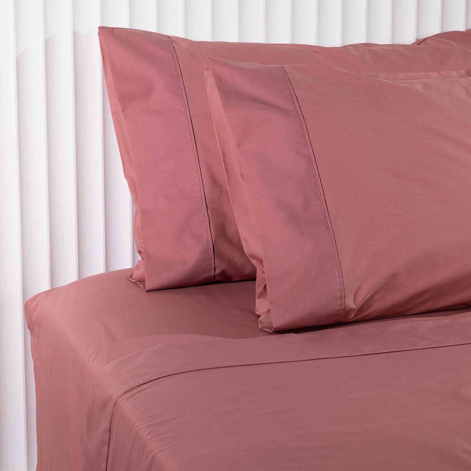 Pink bed sheets and pillowcases on a bed with white headboard