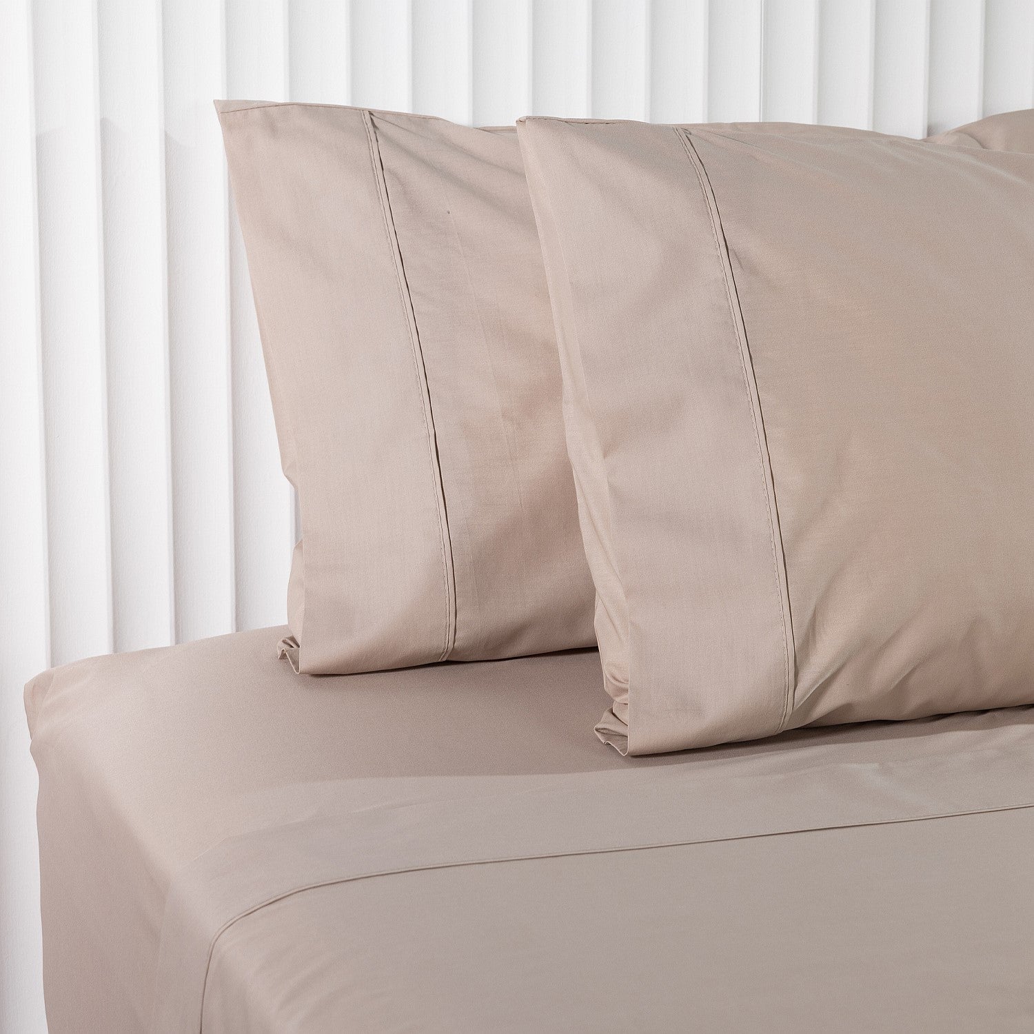 Beige bed flat sheet and pillows on a bed with a white background