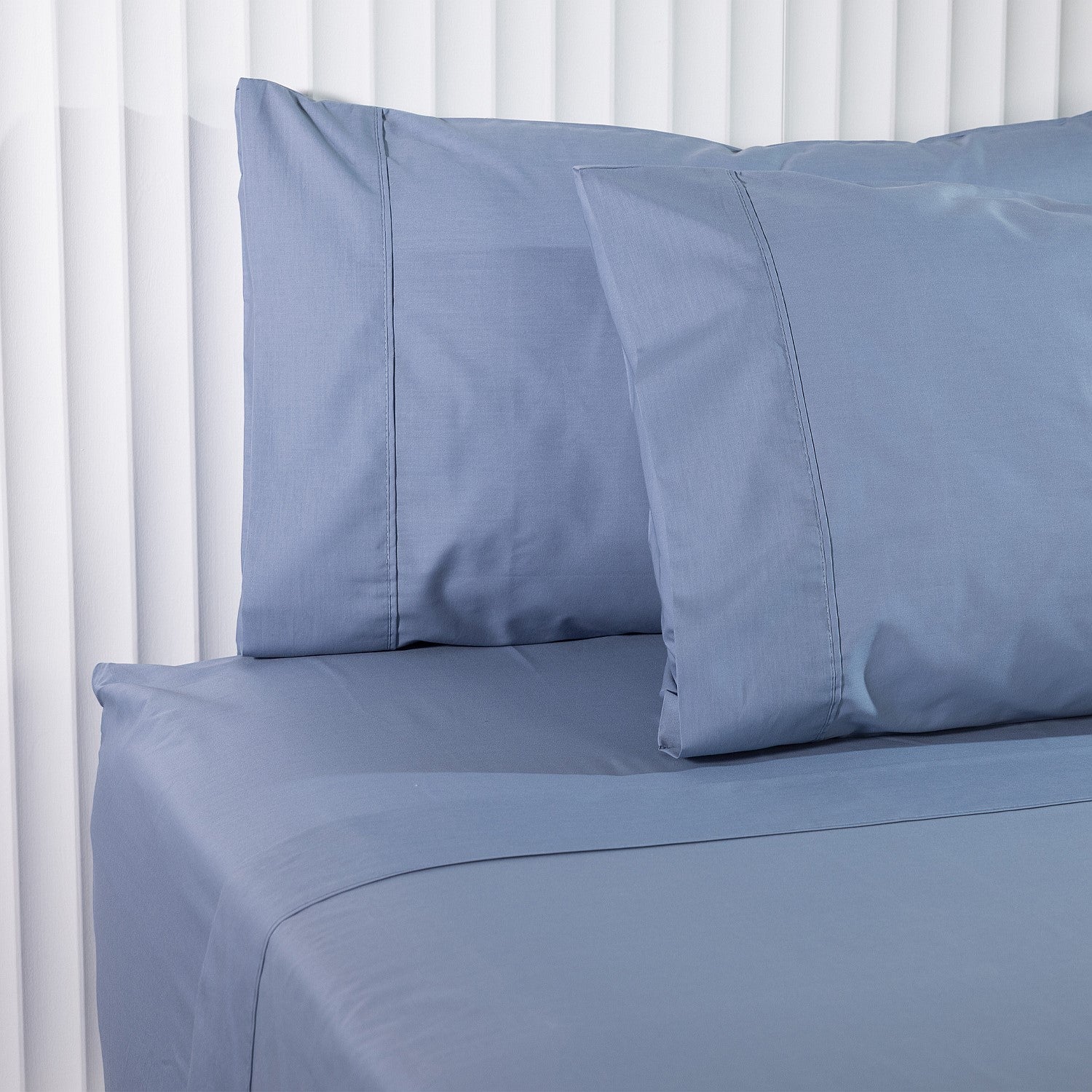 Blue bed sheets and pillowcases on a bed with white bedding in the background