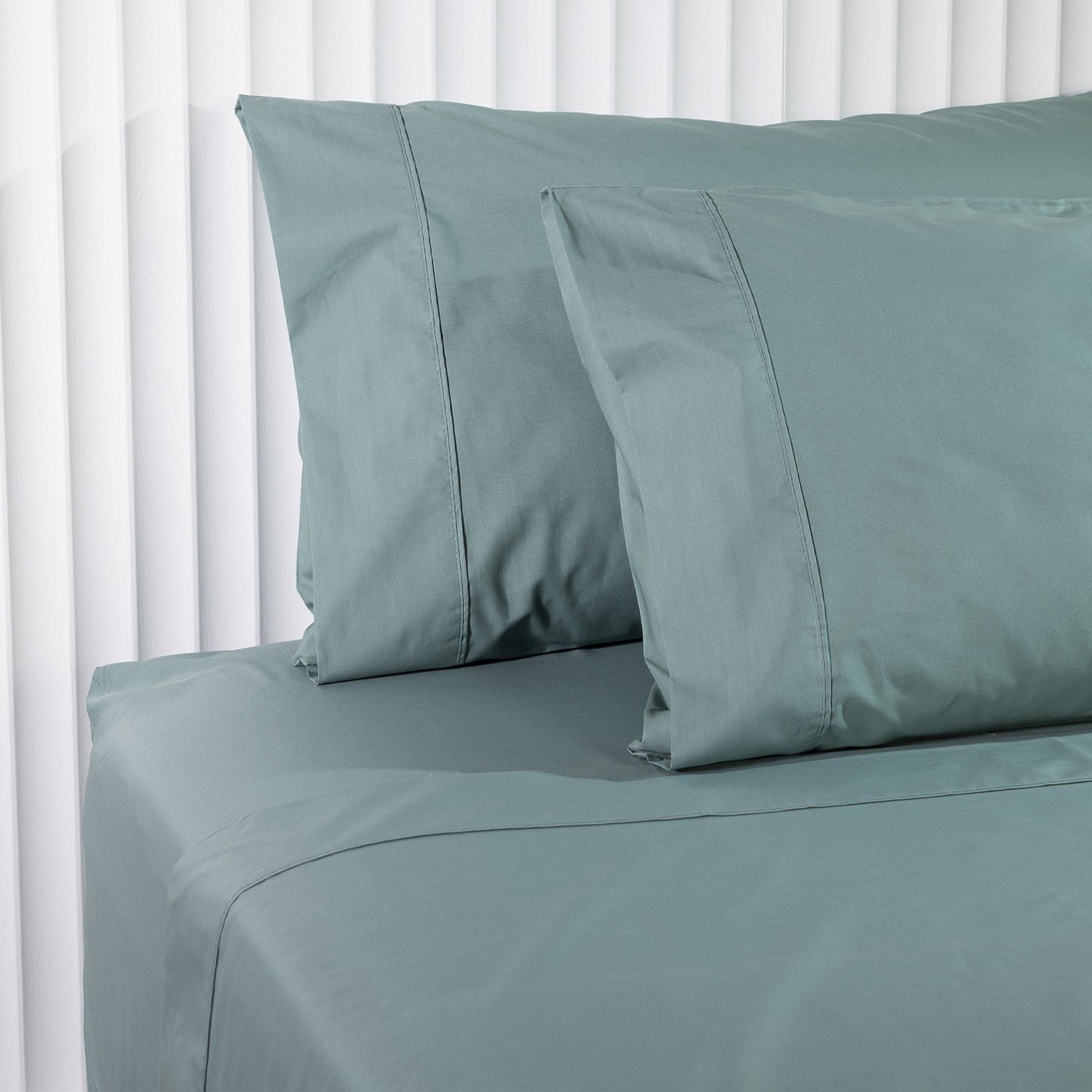 Teal bed sheets and pillowcases on a bed with white vertical blinds in the background.
