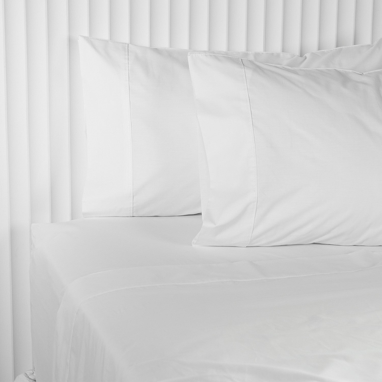 White bed sheets and pillowcases on a bed with a white headboard.