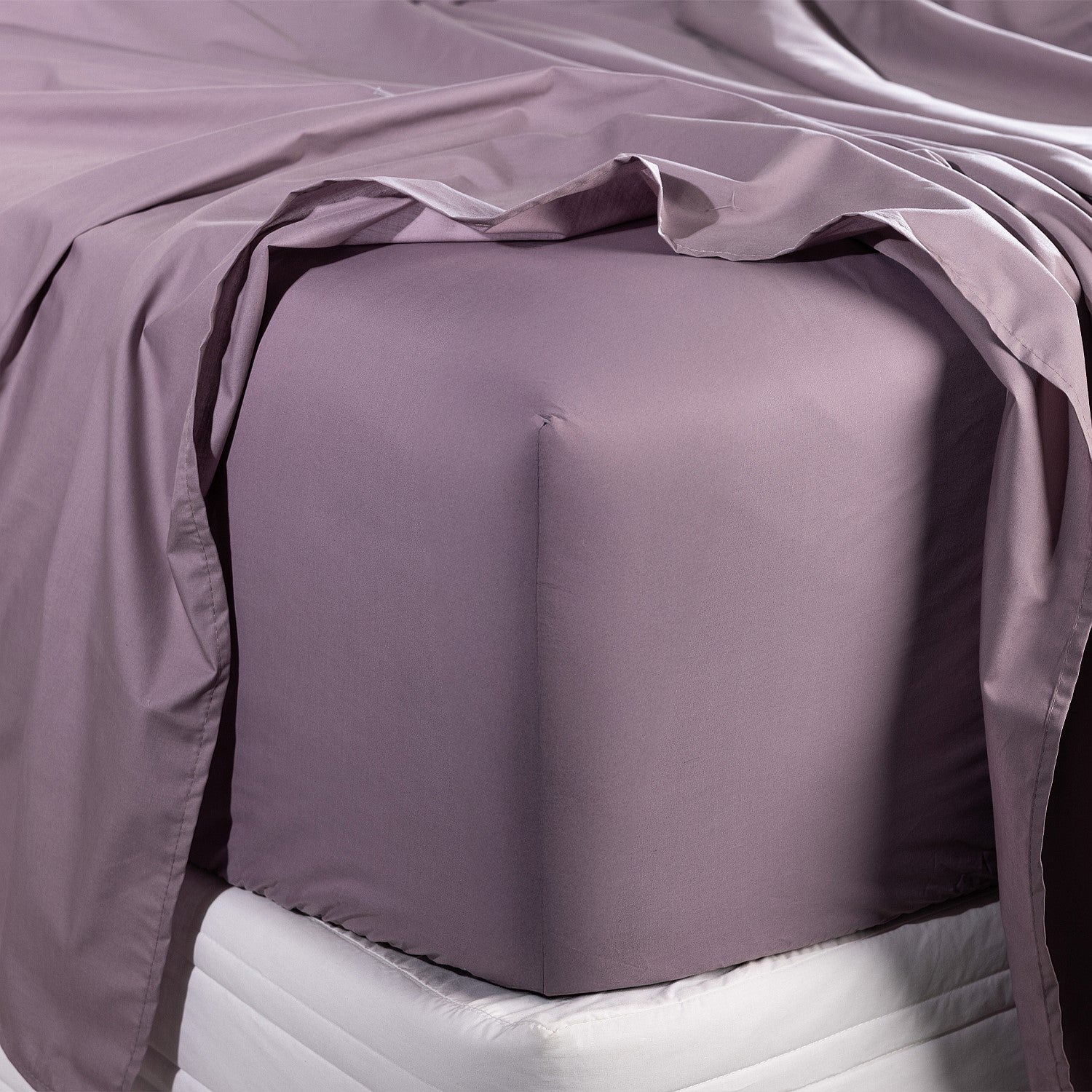 Purple fitted sheet on a bed with a white mattress