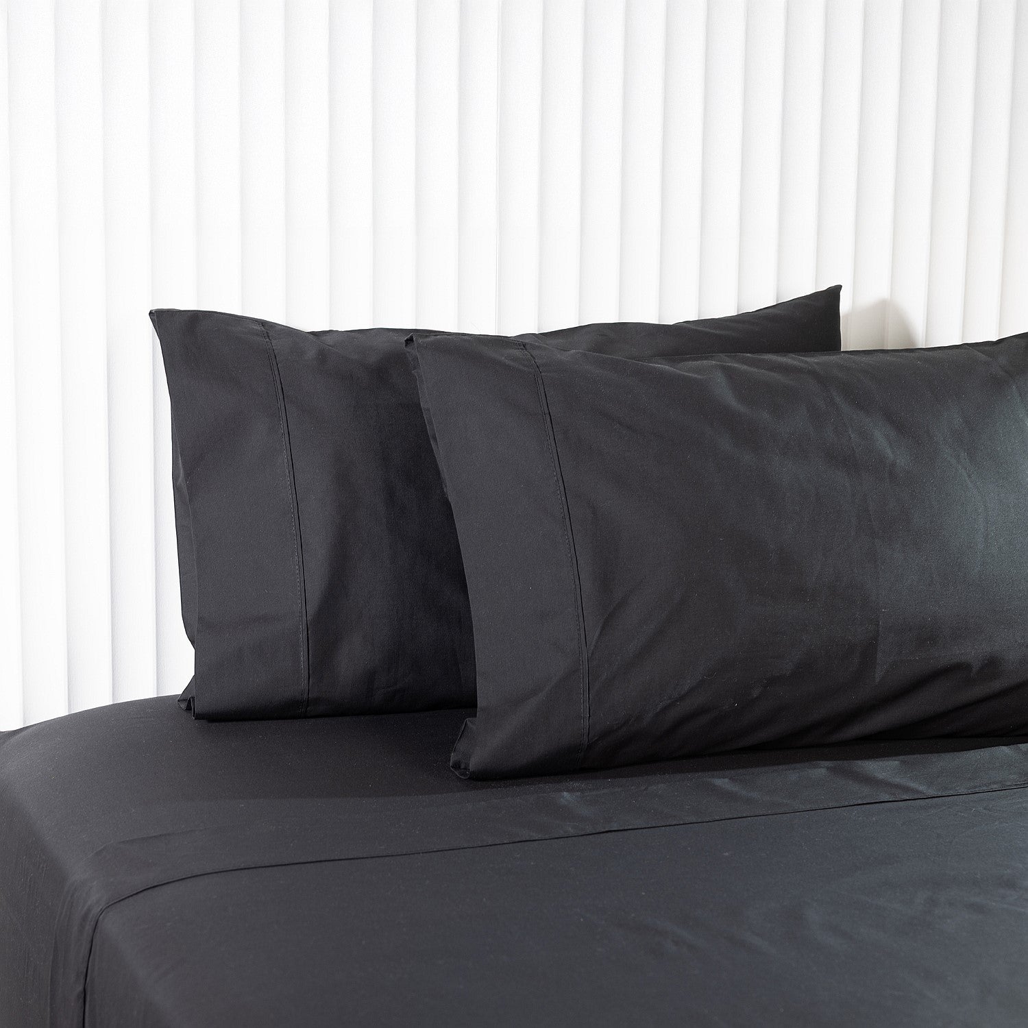 Dark gray bedding set with pillows on a bed against a white background