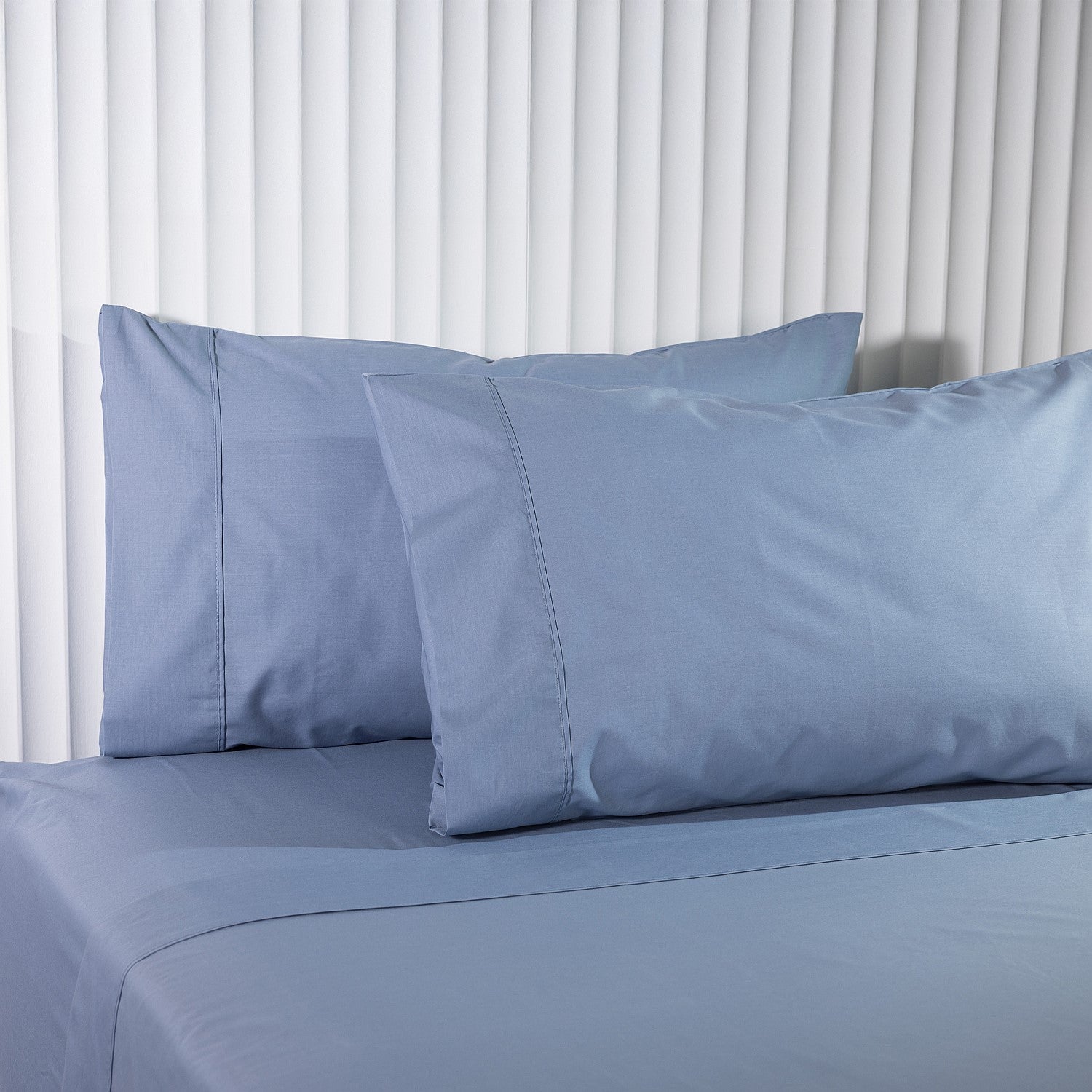 Blue bed sheets and pillows on a bed with white curtains in the background