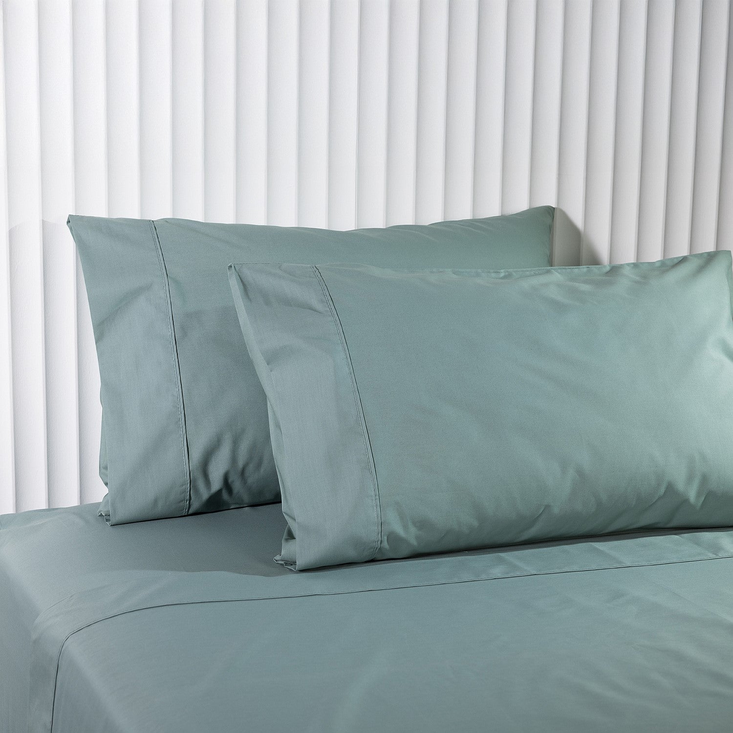 Teal bed sheets and pillowcases on a bed with white curtains in the background