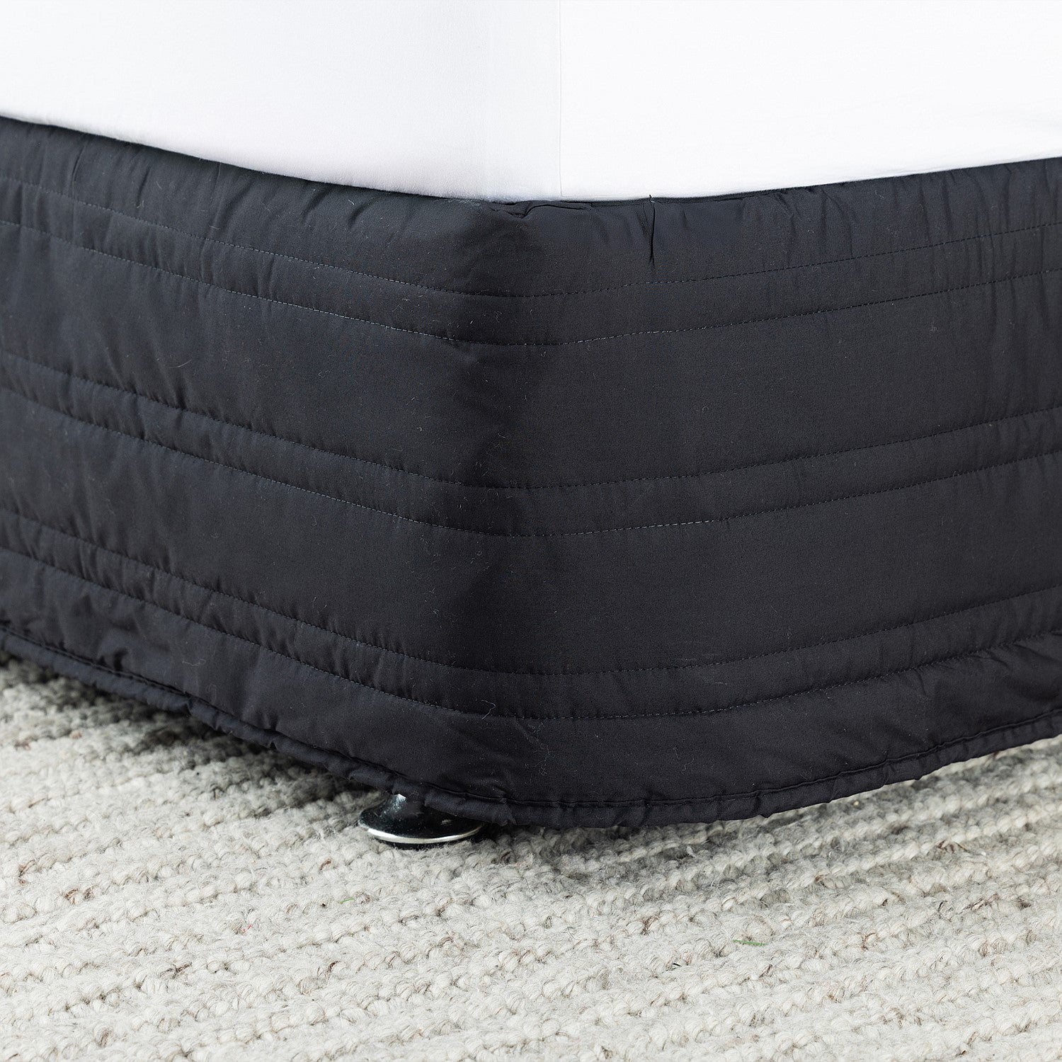 Black quilted mattress cover on a bed with a white mattress.