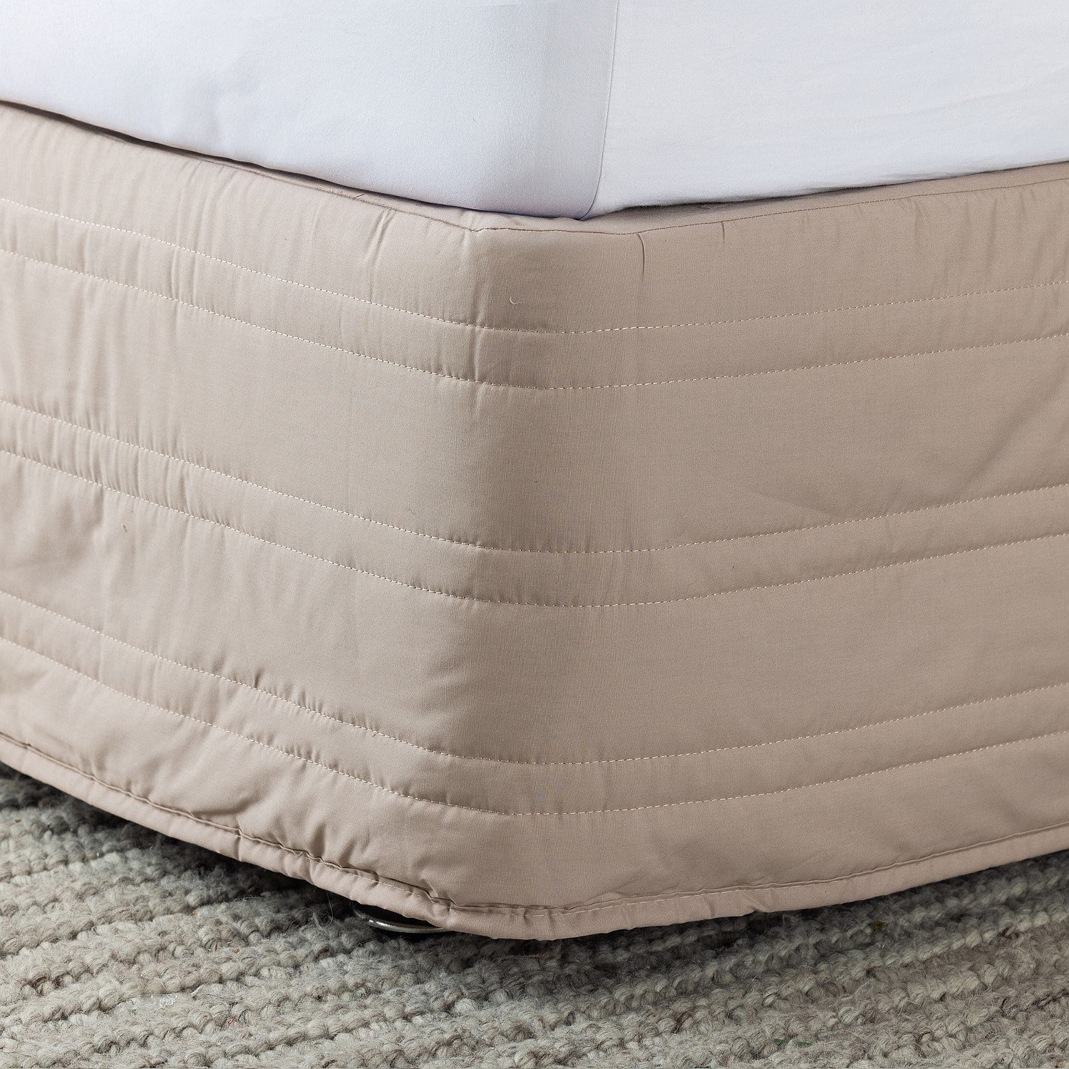 Beige quilted bed skirt on a bed with white bedding.